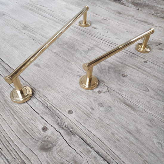 Two Francone BTA31 unlacquered brass linear towel rails with circular brackets on a rustic wood background.