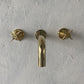 Francone BT48 three-hole wall mounted basin taps with aged brass finish and cross handles installed against a textured white wall.