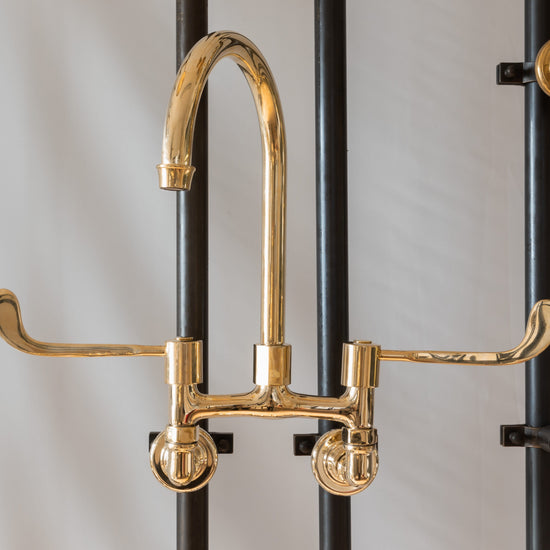 Francone BT49LW wall-mounted kitchen faucet in unlacquered brass with a curved swivel spout and long levers.
