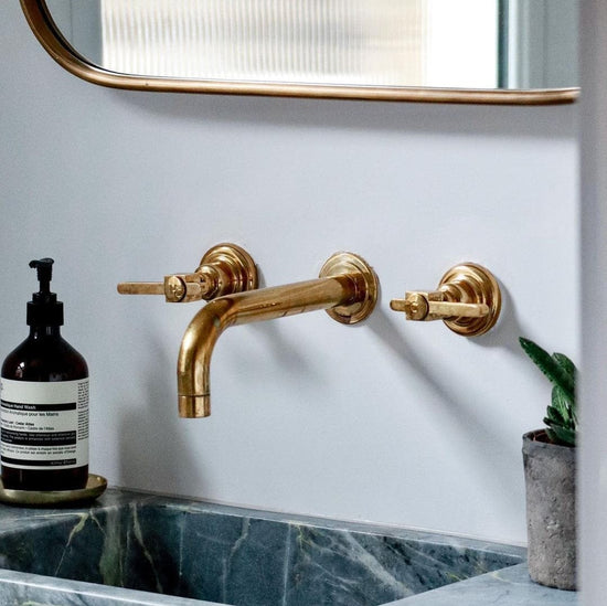 Handcrafted Francone BT58 unlacquered brass wall-mounted basin faucet with lever handles in a bathroom.