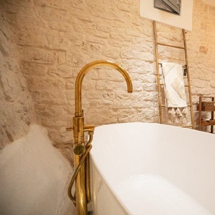 Francone BT87 unlacquered brass floor-mounted bath tap and faucet installed in a rustic stone bathroom.