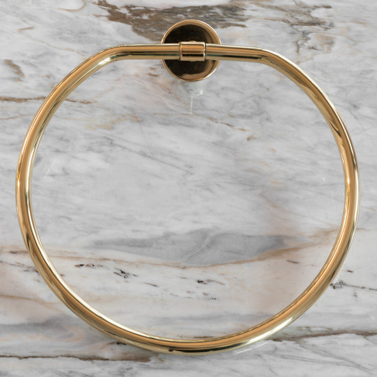 Francone BTA23 circular solid brass towel holder in unlacquered brass, mounted on a marble bathroom wall.