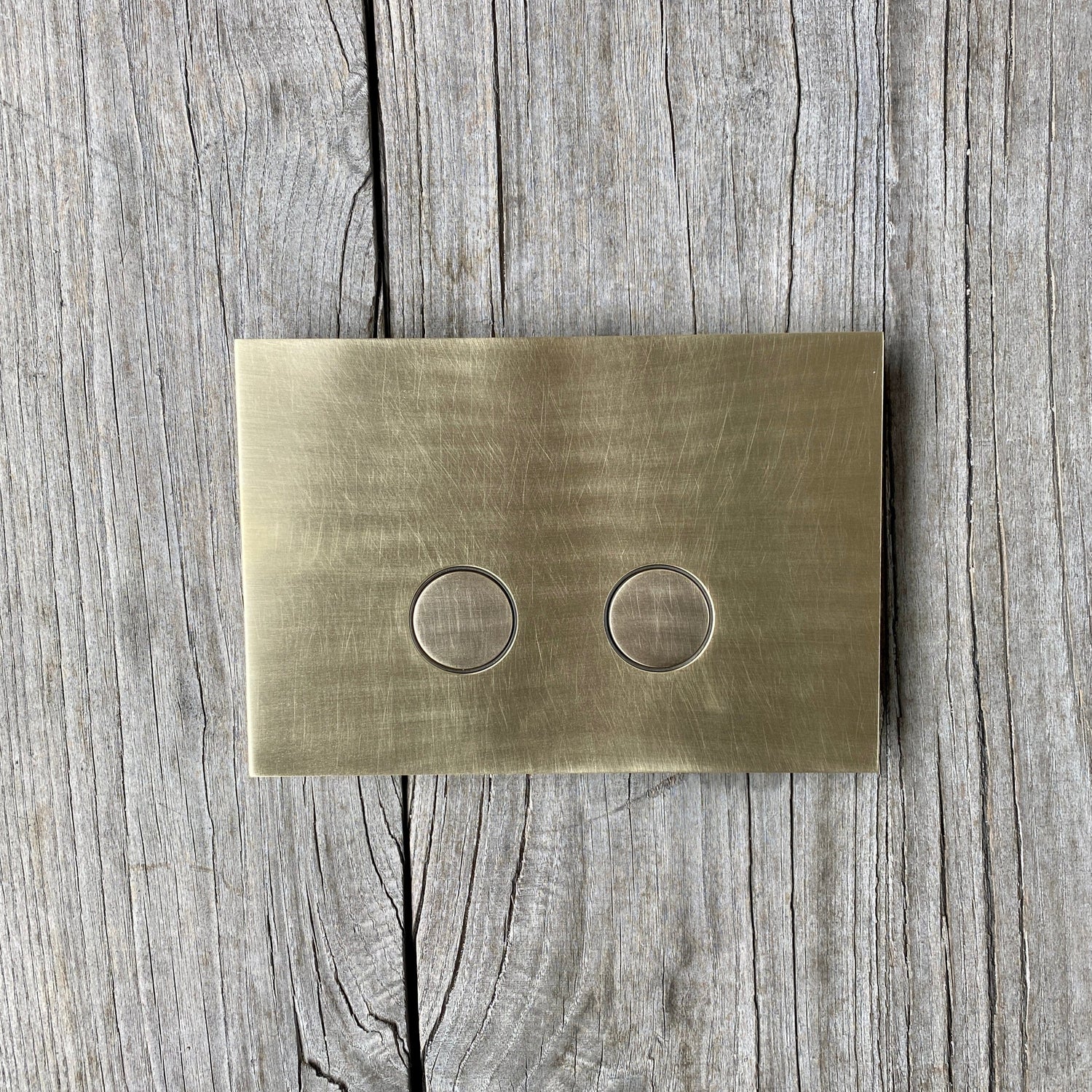 A Francone BTA28 solid brass toilet dual flush plate on a rustic wooden background.