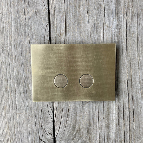 A Francone BTA28 solid brass toilet dual flush plate on a rustic wooden background.