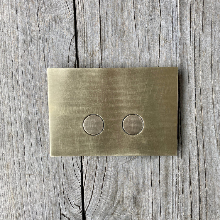 A Francone BTA28 solid brass toilet dual flush plate on a rustic wooden background.