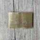 A Francone BTA28 solid brass toilet dual flush plate on a rustic wooden background.