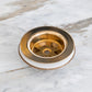 A Francone BTA3 traditional round unlacquered brass kitchen waste plug on a marble countertop.