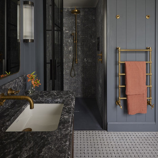 Francone BTR14 solid brass traditional heated towel rail installed on a grey paneled bathroom wall.