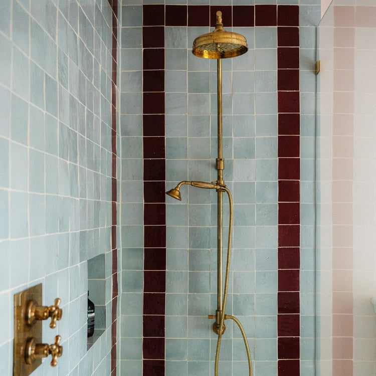 A vintage Francone BTS18 unlacquered brass thermostatic shower column installed in a blue tiled bathroom.