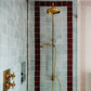 A vintage Francone BTS18 unlacquered brass thermostatic shower column installed in a blue tiled bathroom.