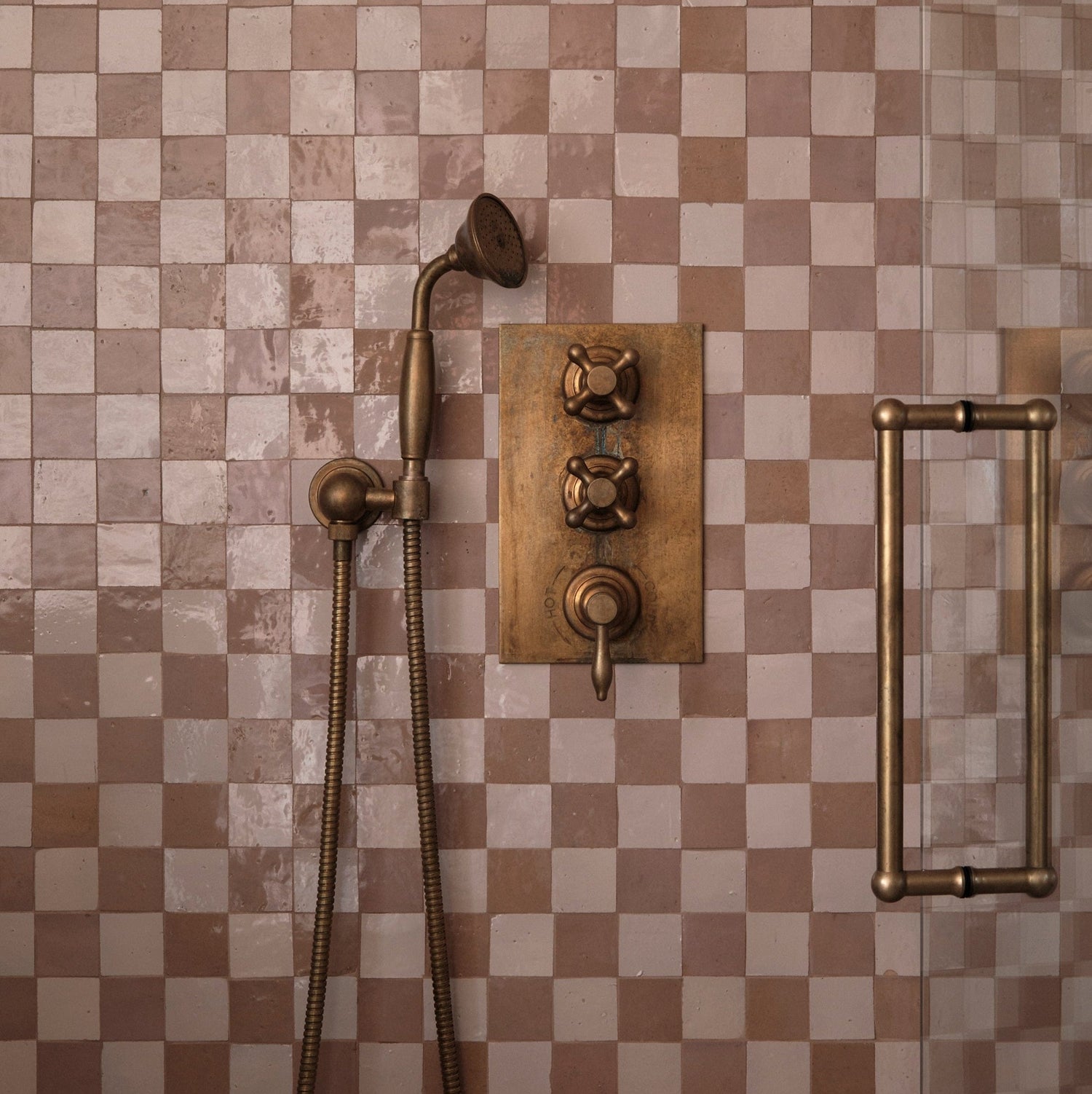 An installed Francone BTS23 wall-mounted hand shower in tumbled brass against check-patterned tiles designed by Millie Turner, photo Sarah Griggs.