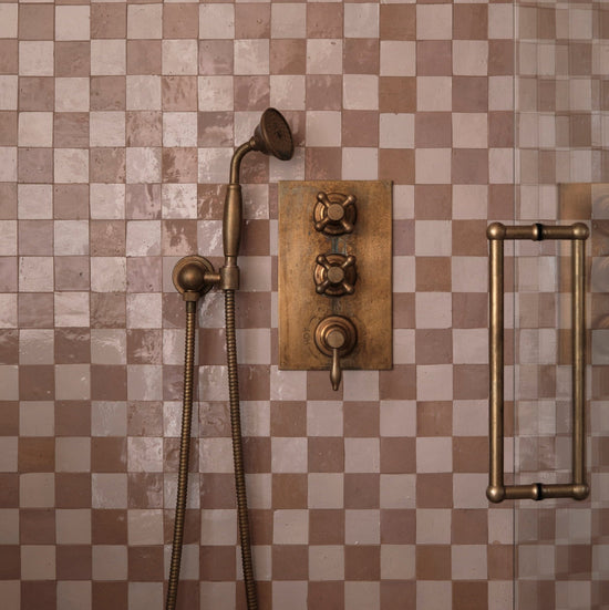 An installed Francone BTS23 wall-mounted hand shower in tumbled brass against check-patterned tiles designed by Millie Turner, photo Sarah Griggs.