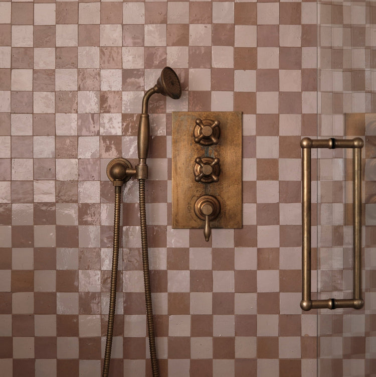 An installed Francone BTS23 wall-mounted hand shower in tumbled brass against check-patterned tiles designed by Millie Turner, photo Sarah Griggs.