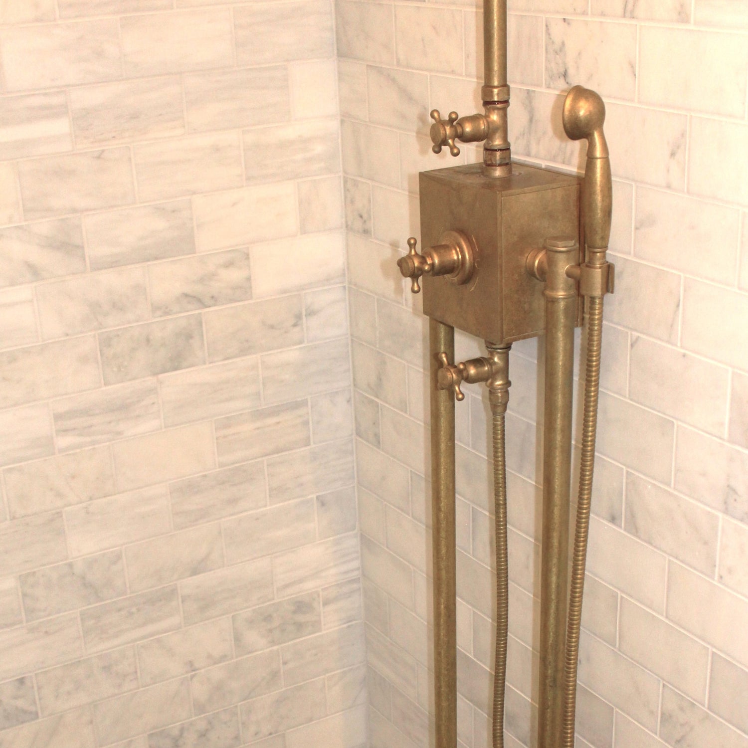 An installed Francone BTS56 thermostatic column shower in unlacquered brass against marble bathroom wall tiles.