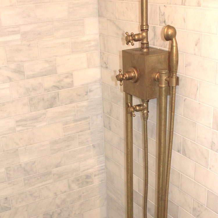 An installed Francone BTS56 thermostatic column shower in unlacquered brass against marble bathroom wall tiles.