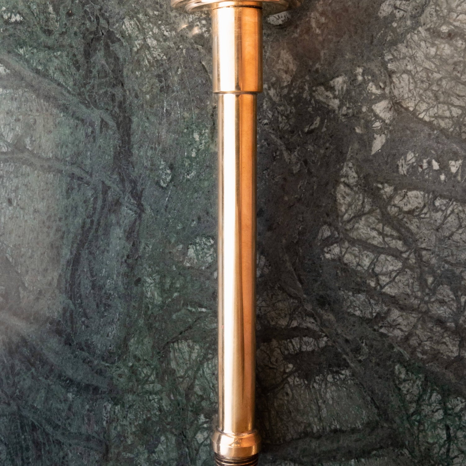 A Francone BTSA solid brass ceiling-mounted shower arm in unlacquered brass against a green marble wall.