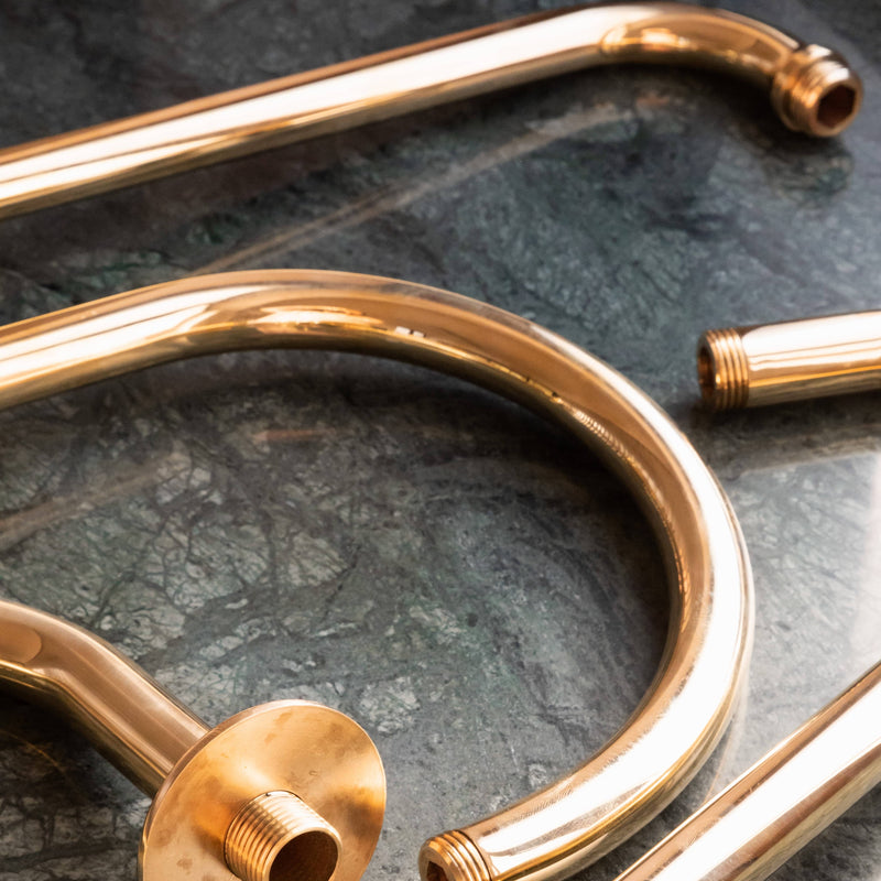 Francone BTSA unlacquered brass curved shower arms with a living finish on green marble.