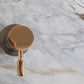 Close-up of the circular solid brass handle for the Francone SSS17 shower mixer, mounted on a marble wall.