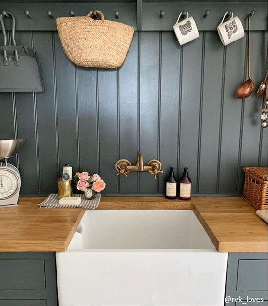 Francone BT40 wall mounted traditional solid brass tap above a white farmhouse sink with dark green paneled walls and a wooden countertop.