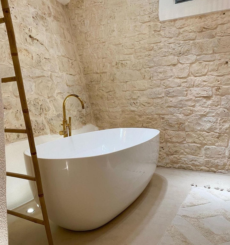 An installed Francone BT87 unlacquered brass floor-mounted bath tap and faucet next to a white tub.