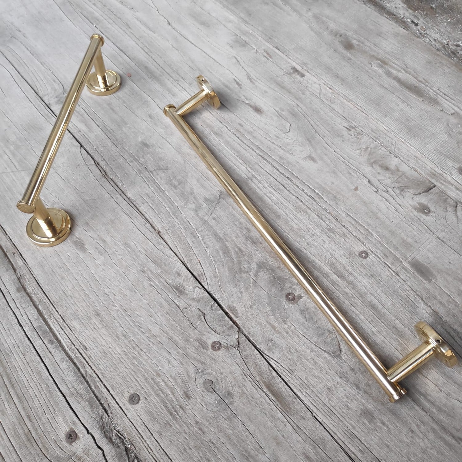 Two Francone BTA24 and BTA31 solid unlacquered brass towel rails on a rustic wooden background.