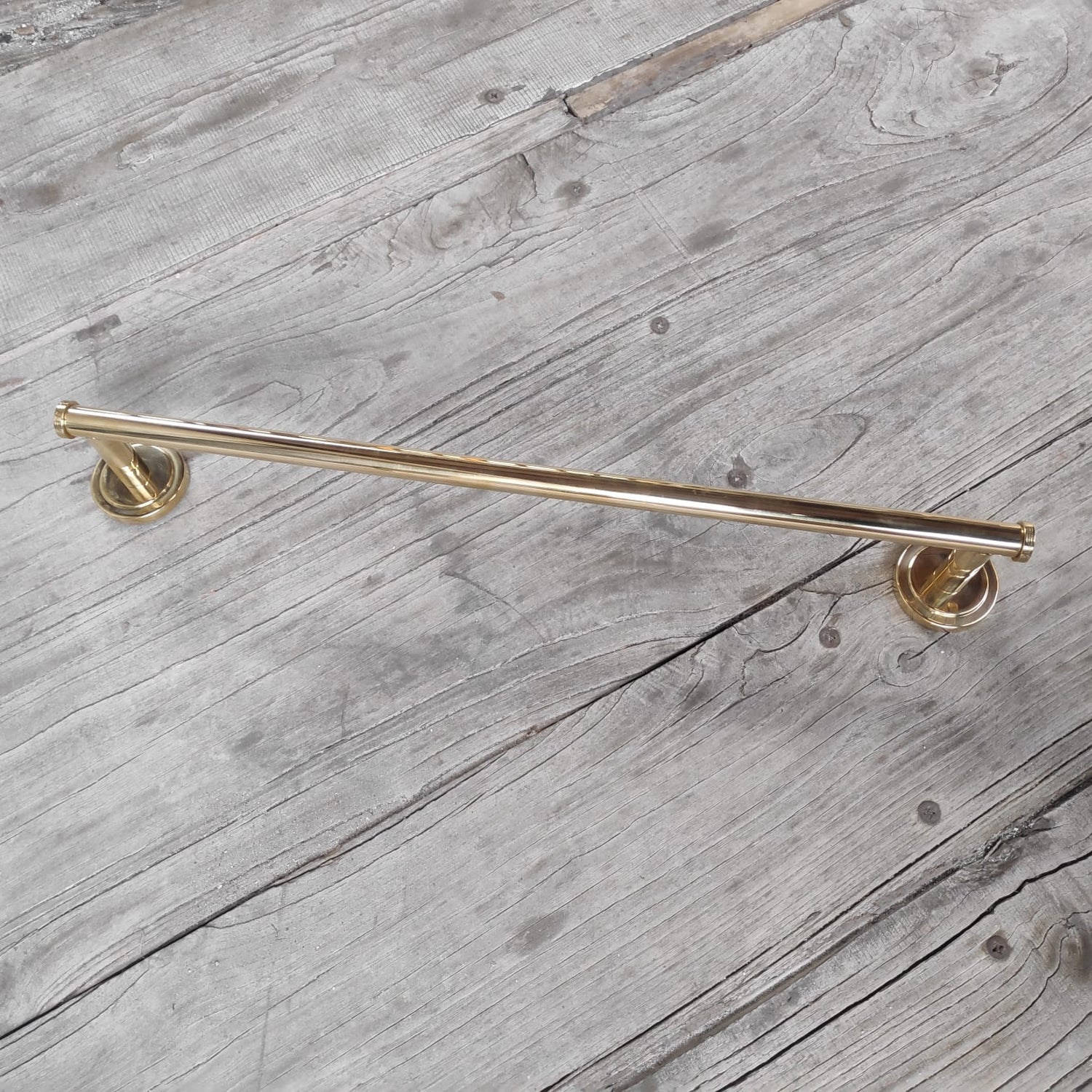 A bespoke Francone BTA24 solid unlacquered brass linear bathroom towel rail on a rustic wood surface.