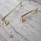 Two Francone BTA31 unlacquered brass linear towel rails with circular brackets on a rustic wood background.