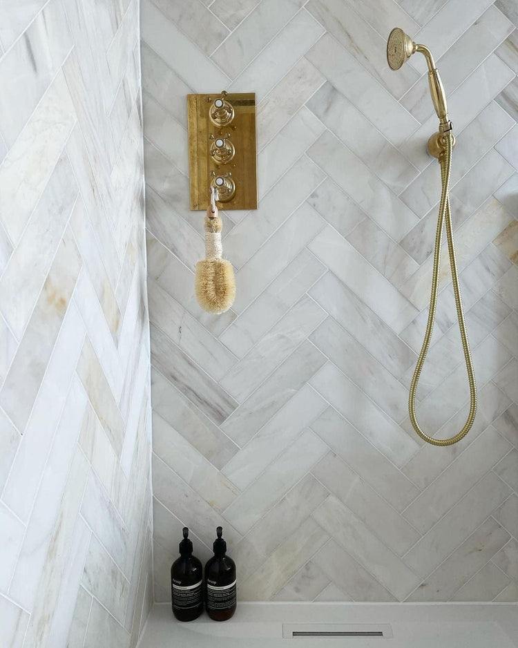 Francone BTS23 unlacquered brass wall-mounted hand shower installed on white marble herringbone tile by Victoria at the White Cottage.