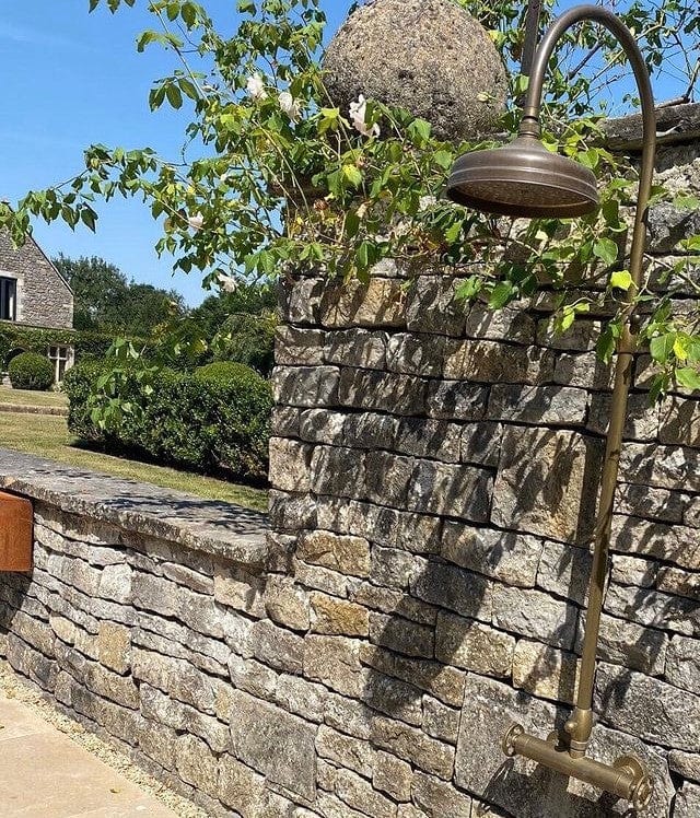 The Francone BTS47 thermostatic column shower in solid brass installed as an outdoor shower against a rustic stone wall.