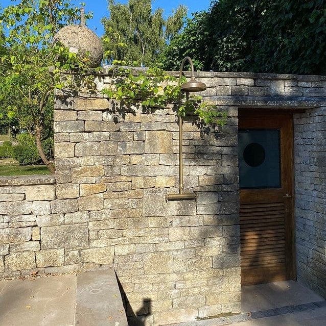 Francone BTS47 unlacquered brass thermostatic column shower installed on an outdoor stone wall.